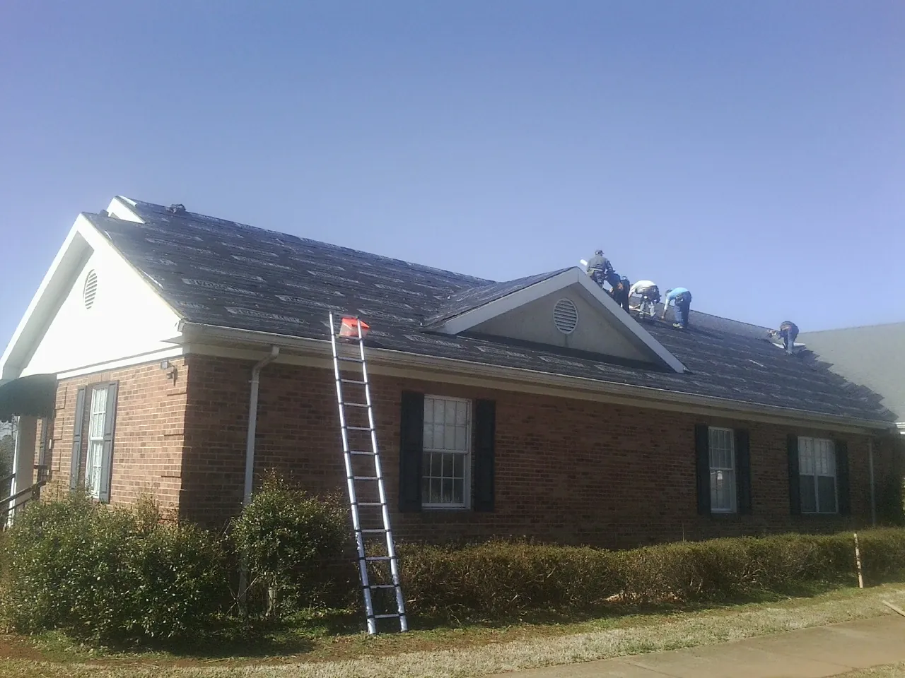 Crew tearing shingles off a brick ranch roof with a ladder set — Metal Roof Repair work by our crew in Black Mountain