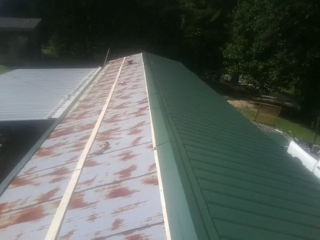 Old rusted panels beside newly installed green metal roofing — Wind Damage Roof Repair by Roofing Brothers in Black Mountain