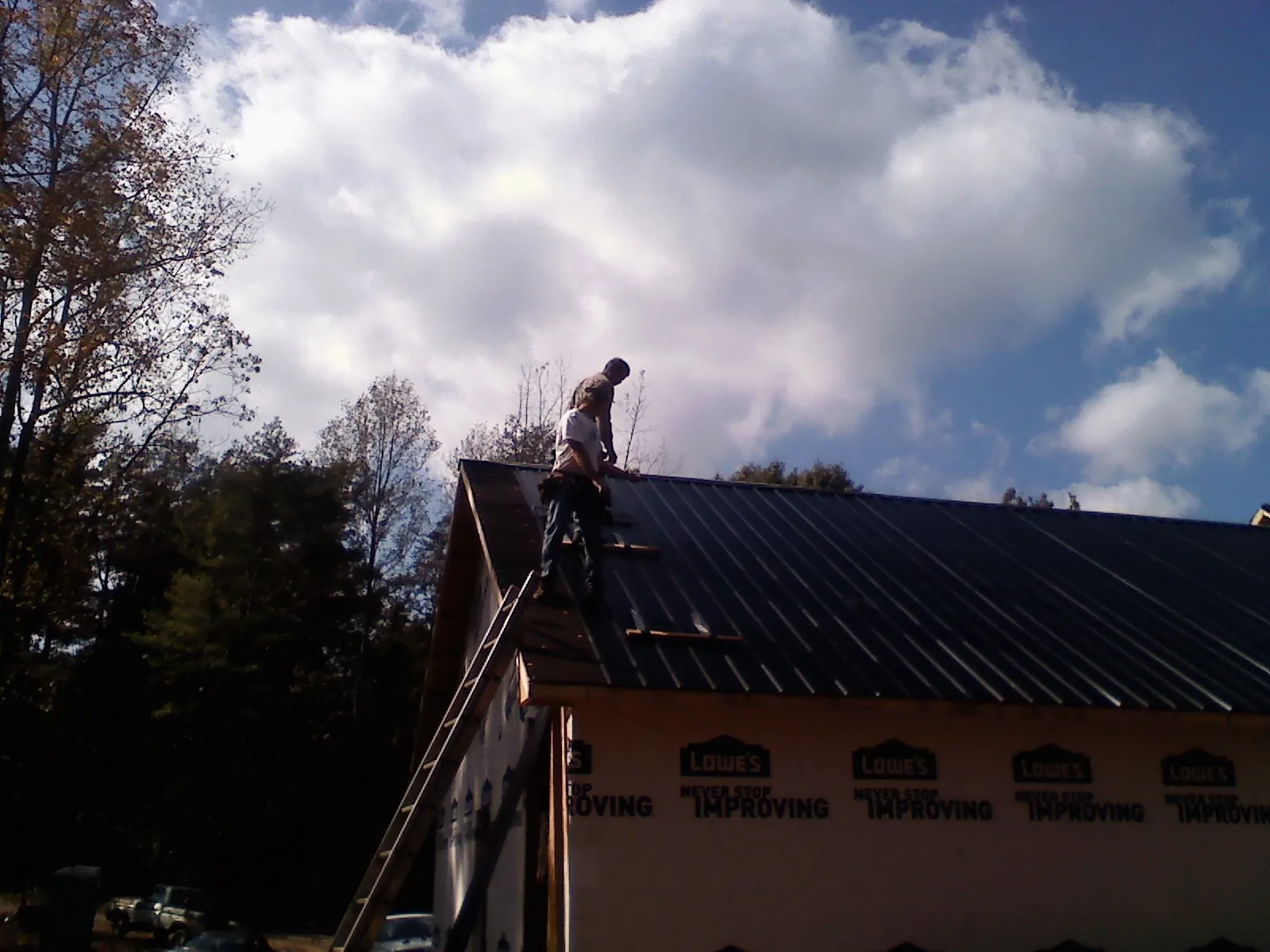 Roofer fastening dark metal panels high against a cloudy sky, from a Roof Inspection job in Black Mountain