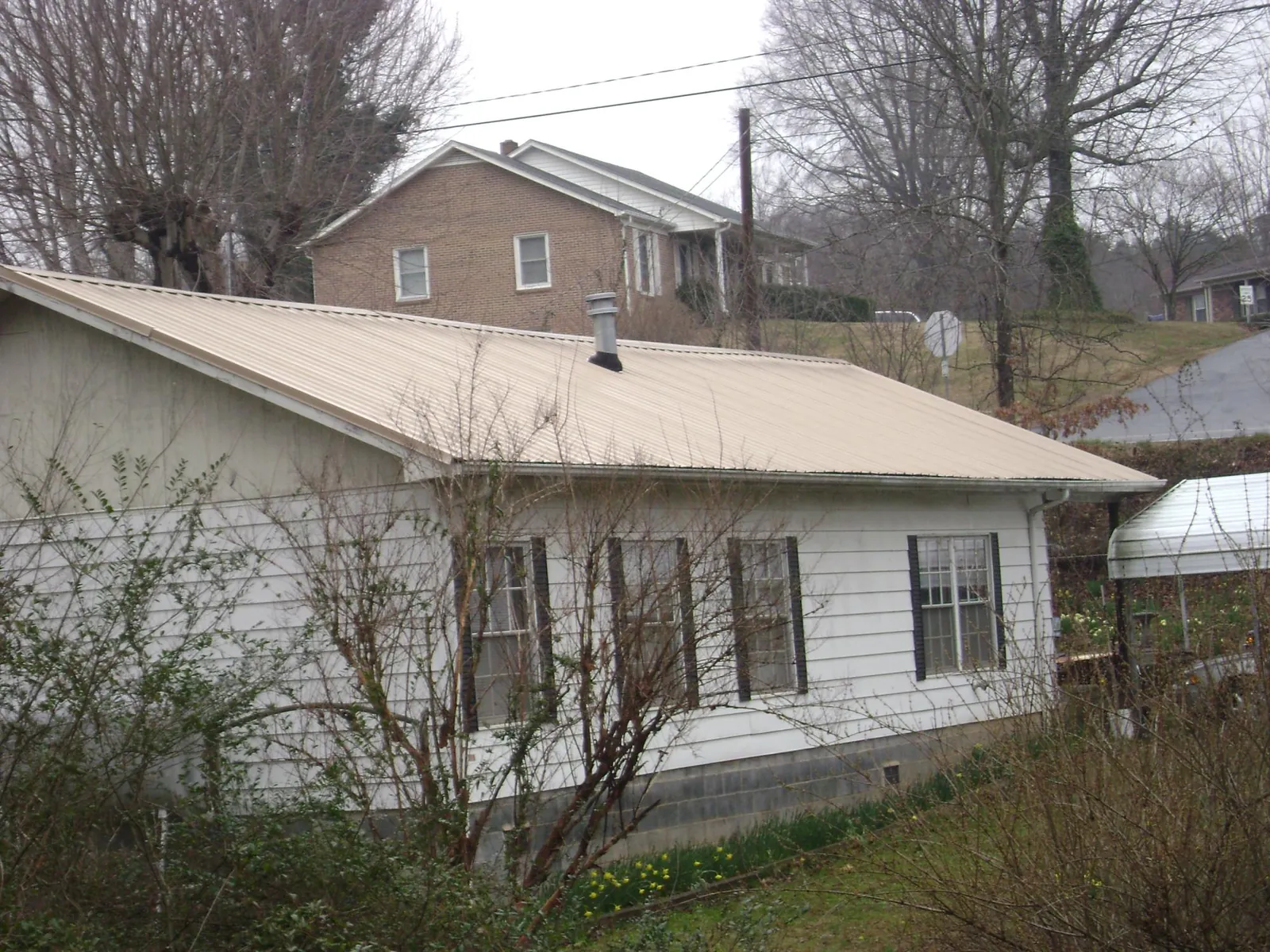 Tan metal roof on a white sided house set into a hillside — Commercial Roofing by Roofing Brothers in Black Mountain