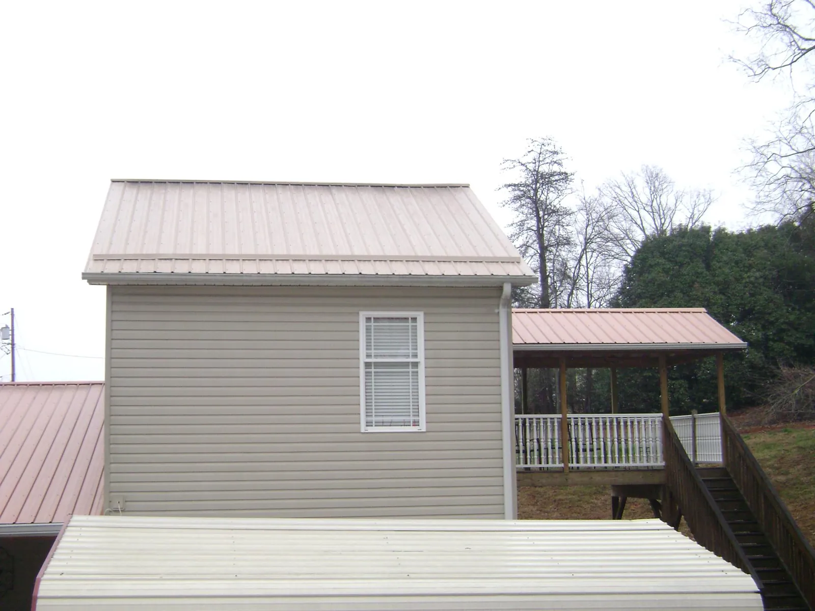 Tan metal roofs on a two story addition and attached porch, from a Roof Replacement job in Black Mountain